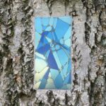 Rectangular blue geometric mosaic panel mounted on rough tree bark.