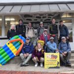 Group of hikers posing on the steps outside an Appalachian Trail Conservancy building, with a colorful inflatable raft and a Flip Flop Festival sign nearby.