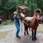 A man places a pack saddle onto a mule.