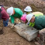 Group of volunteers wearing PPE heaves a large stone boulder into place along the Appalachian Trail.