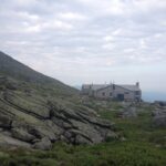 A wooden structure stands at a mountain overlook amid rocky alpine terrain.
