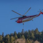 Helicopter hovers above a forested mountain with a line hanging beneath it.